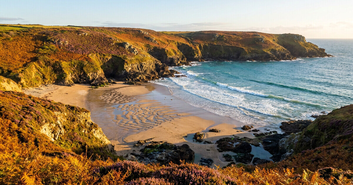 A deserted sandy cove on the British coast in autumn sunlight, with bracken-covered cliffs and turquoise sea.